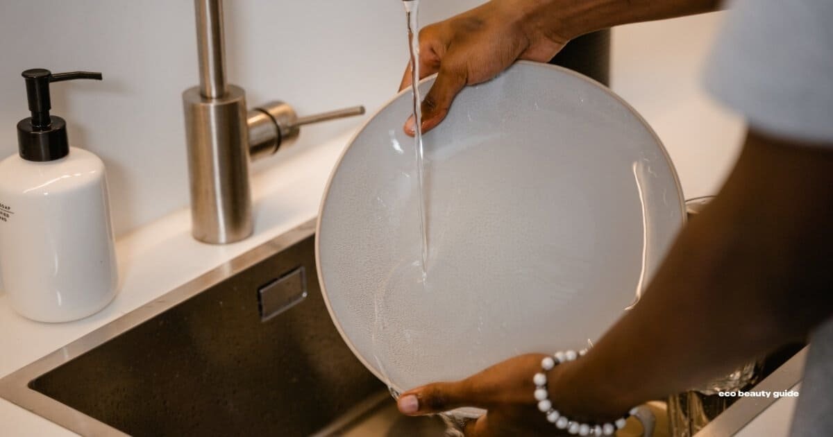 A person washing a plate in the kitchen sink.