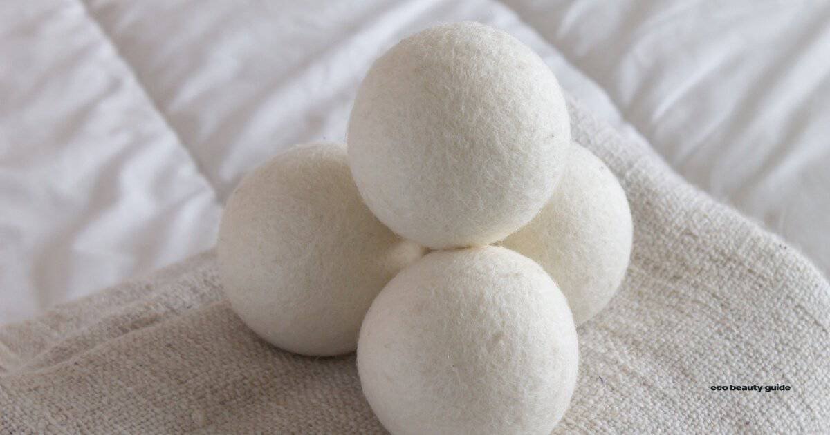 Four white wool balls for cruelty-free dryer sheets on a bed.